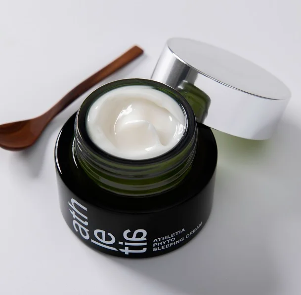 Athletia Phyto Sleeping Cream jar opened with a wooden spatula beside it. The rich, white cream texture highlights the product’s botanical formulation, featuring plant-derived oils such as olive, primrose, and grapeseed for deep overnight hydration.